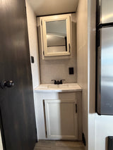 Compact RV rental interior featuring a bathroom vanity with sink and mirror, next to a refrigerator, optimizing space.