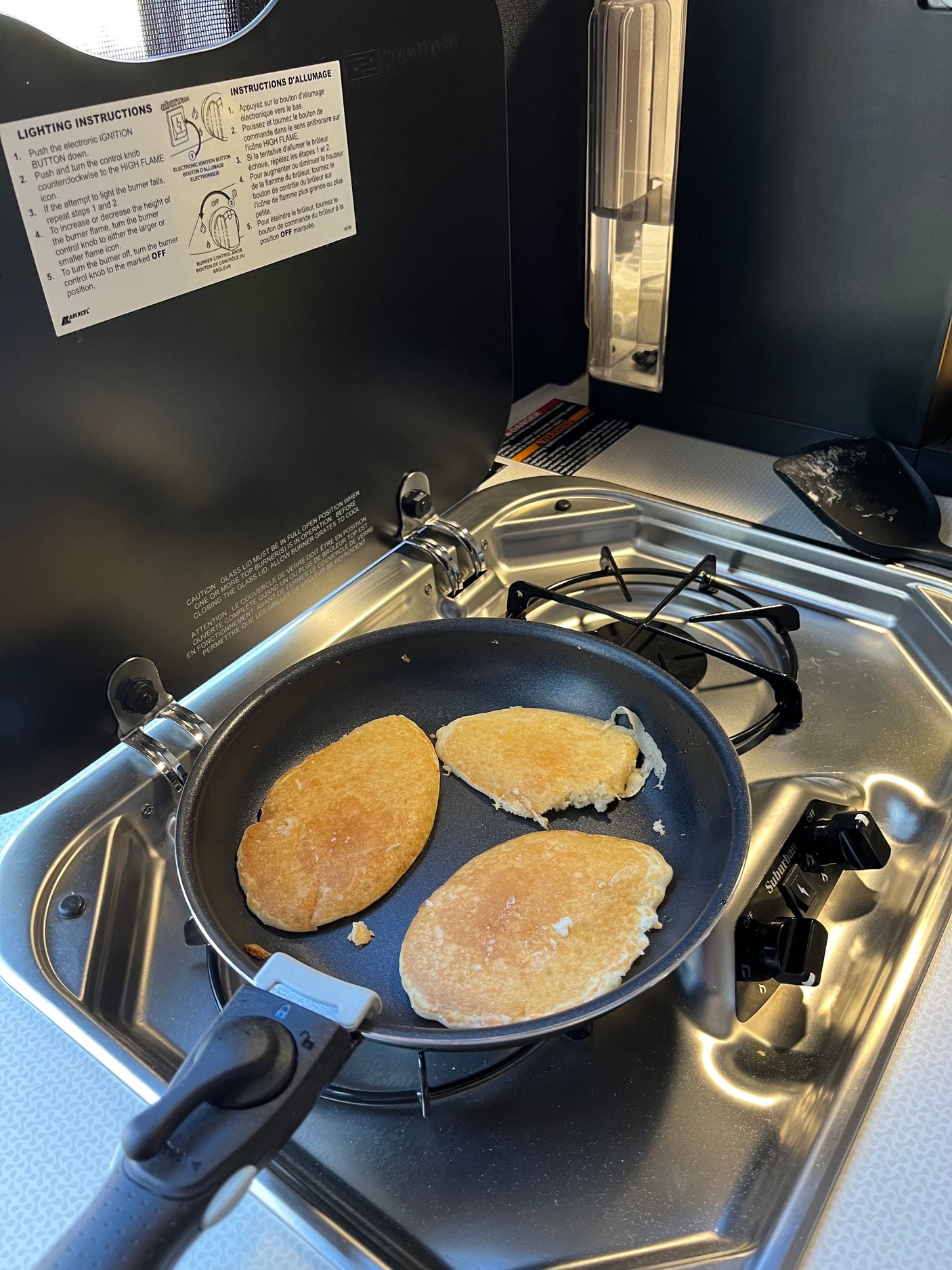 Fresh pancakes sizzling on a compact stovetop in an RV rental kitchen, with burner instructions clearly visible.
