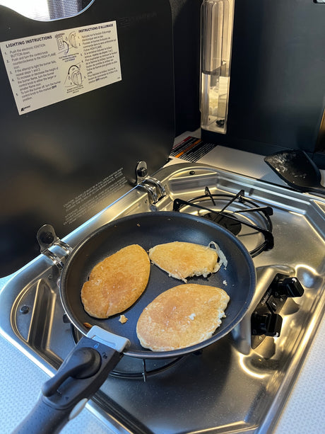 Fresh pancakes sizzling on a compact stovetop in an RV rental kitchen, with burner instructions clearly visible.