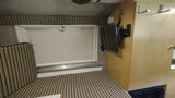 RV rental: Interior shows a cozy bed/seating with patterned fabric, a window, wall-mounted TV, and wood cabinetry.