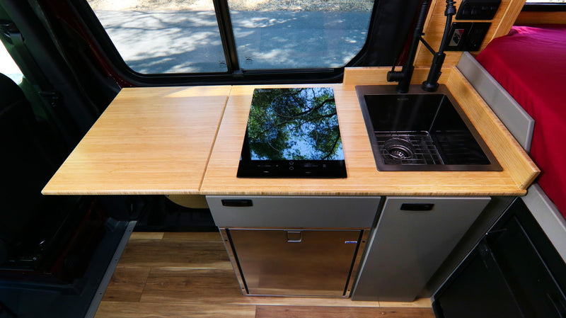  surrounded by green trees.|This RV rental interior showcases a modern camper van with a compact kitchen — photo 6