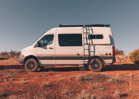 White Storyteller Overland 4x4 RV rental parked on a vibrant red dirt road under a clear sky, ready for adventure.