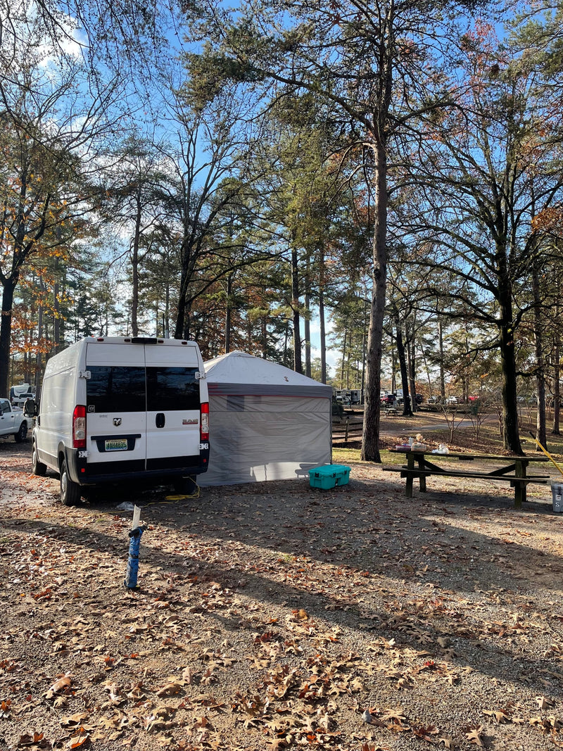 White rv rental van with a tent and picnic table at a scenic fall campsite in a forest, surrounded by autumn leaves. — photo 17