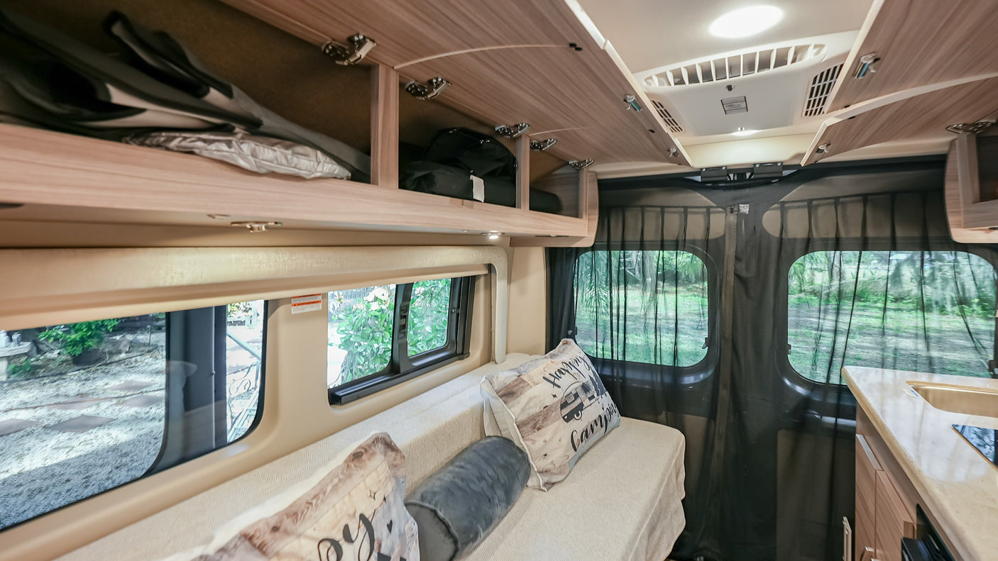 Experience adventure in this RV rental! Interior shows a comfortable seating/sleeping area, storage, and kitchenette.