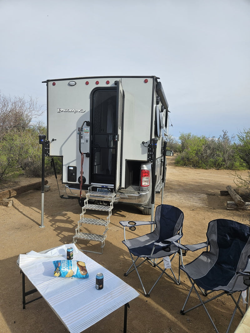 Relaxing at a sandy campsite with an rv rental Palomino truck camper, featuring chairs, table, and snacks. — photo 13