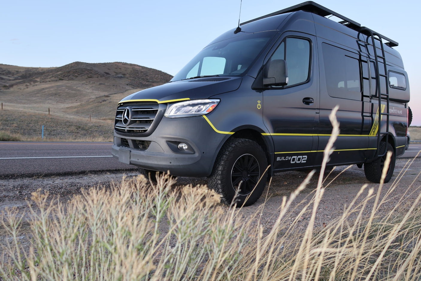 Dark grey Mercedes Sprinter adventure van (BUILD#002) with yellow accents, an ideal rv rental for exploring scenic roads.