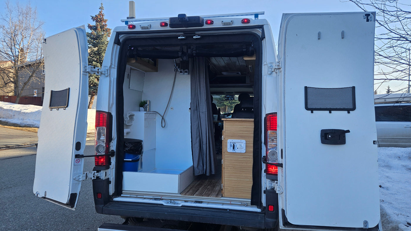 Open rear doors of an RV rental show a custom camper van interior with a built-in shower, sink, and storage for comfortable van life. — photo 13