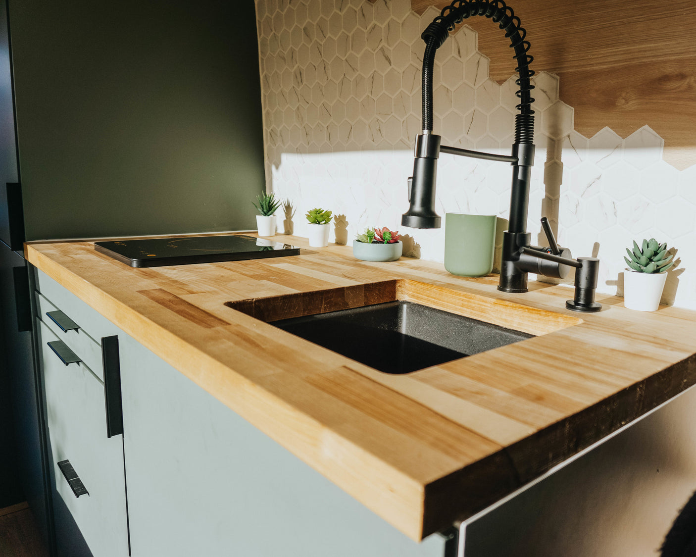 Modern RV rental kitchen featuring wood counters, a black sink, induction cooktop, and sleek tiled backsplash.