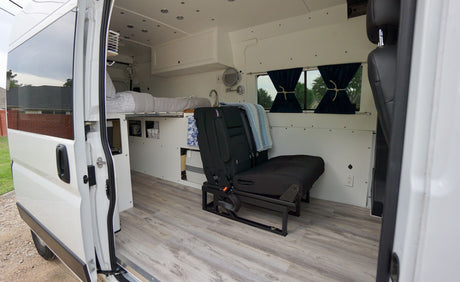 View inside an rv rental campervan, showcasing an elevated bed, convertible bench seat, and sink area.