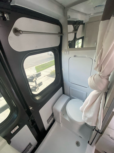 Compact RV rental bathroom with toilet, shower area, and window views. Ideal for camper travel.