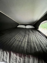 Cozy RV rental pop-top bed with a dark quilted comforter and two striped pillows, offering comfort for your travels.