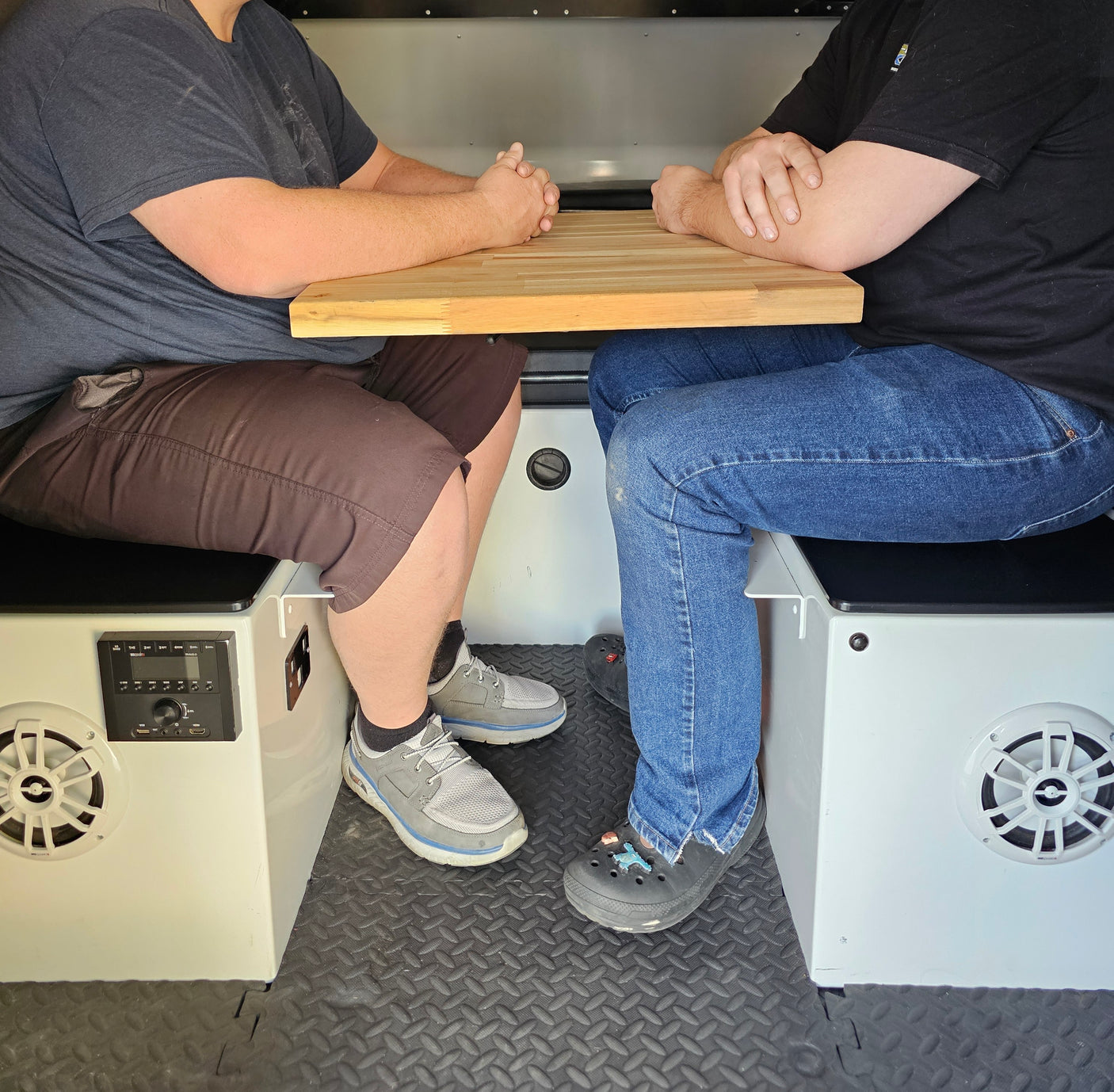 RV rental interior: Two people at a compact table with integrated stereo, ideal for travel and adventure.