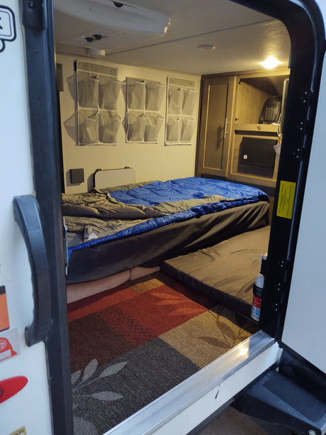Inside a cozy RV rental: bed, wall organizers, and safety equipment for comfortable camping trips.