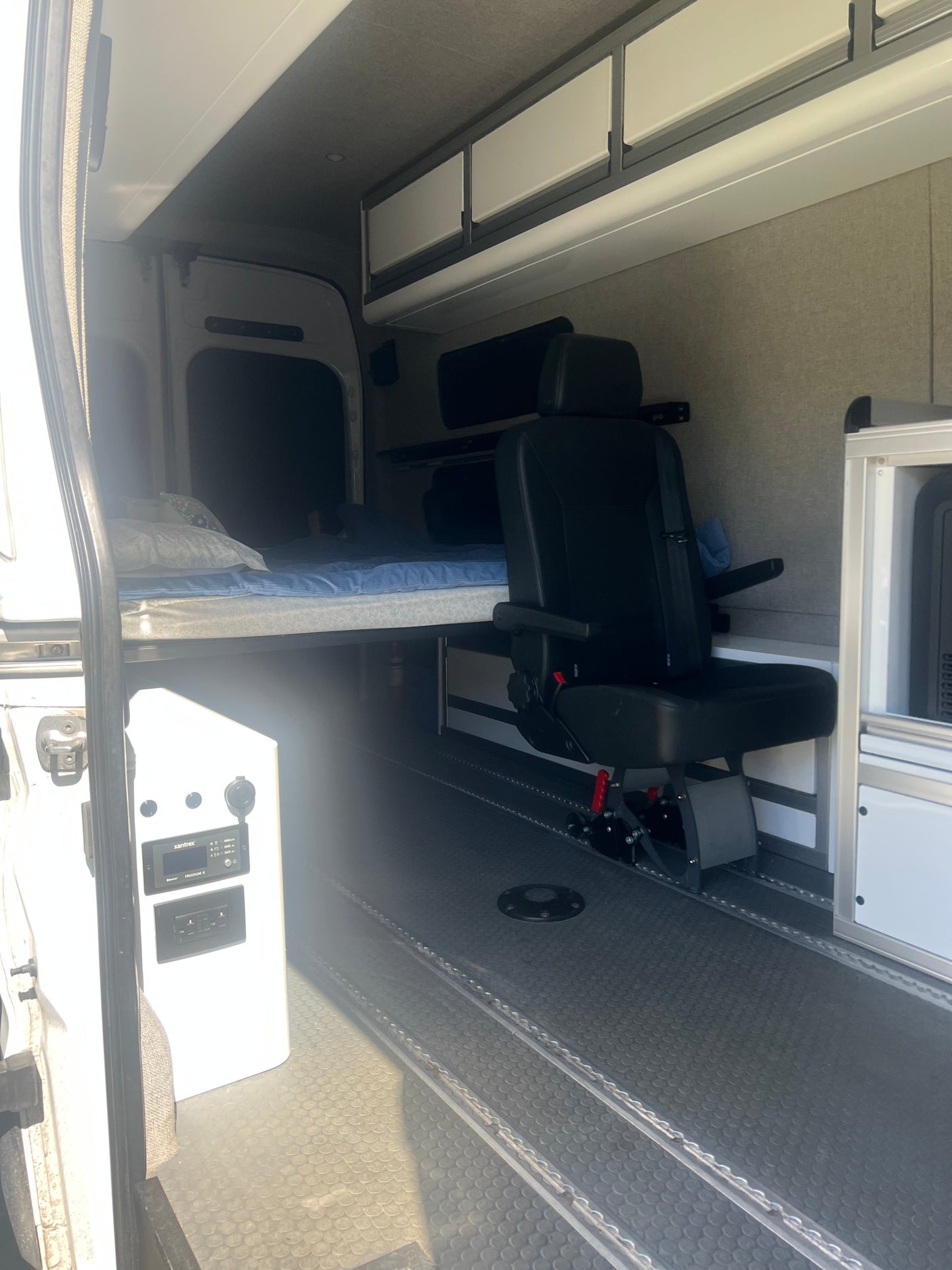 Inside this rv rental van: a comfy bed, swivel passenger seat, overhead cabinets, and power control panel.