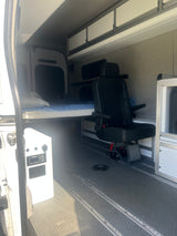 Inside this rv rental van: a comfy bed, swivel passenger seat, overhead cabinets, and power control panel.