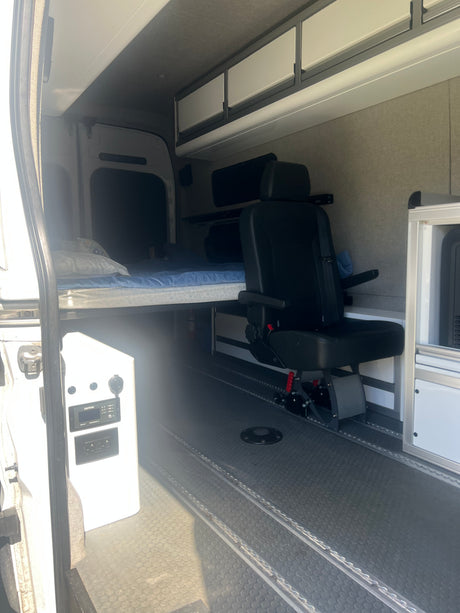 Inside this rv rental van: a comfy bed, swivel passenger seat, overhead cabinets, and power control panel.