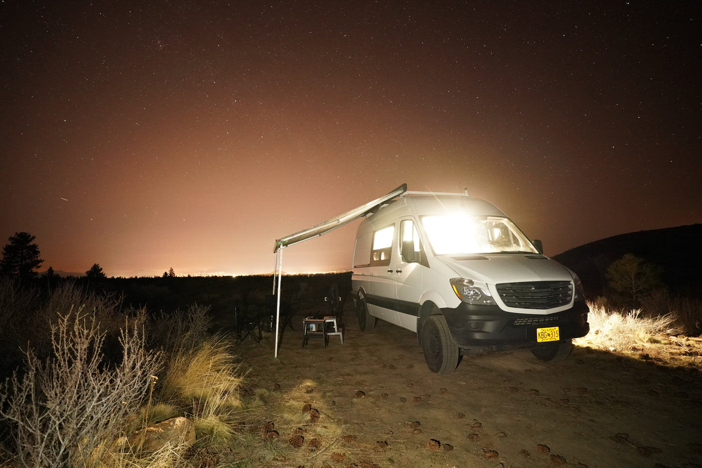 Night adventure with an RV rental! White Sprinter van, lights glowing under a clear, starry sky, parked for remote camping.