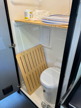 RV rental wet bath: compact space with toilet, wooden mat, and a shelf holding RV tank supplies.