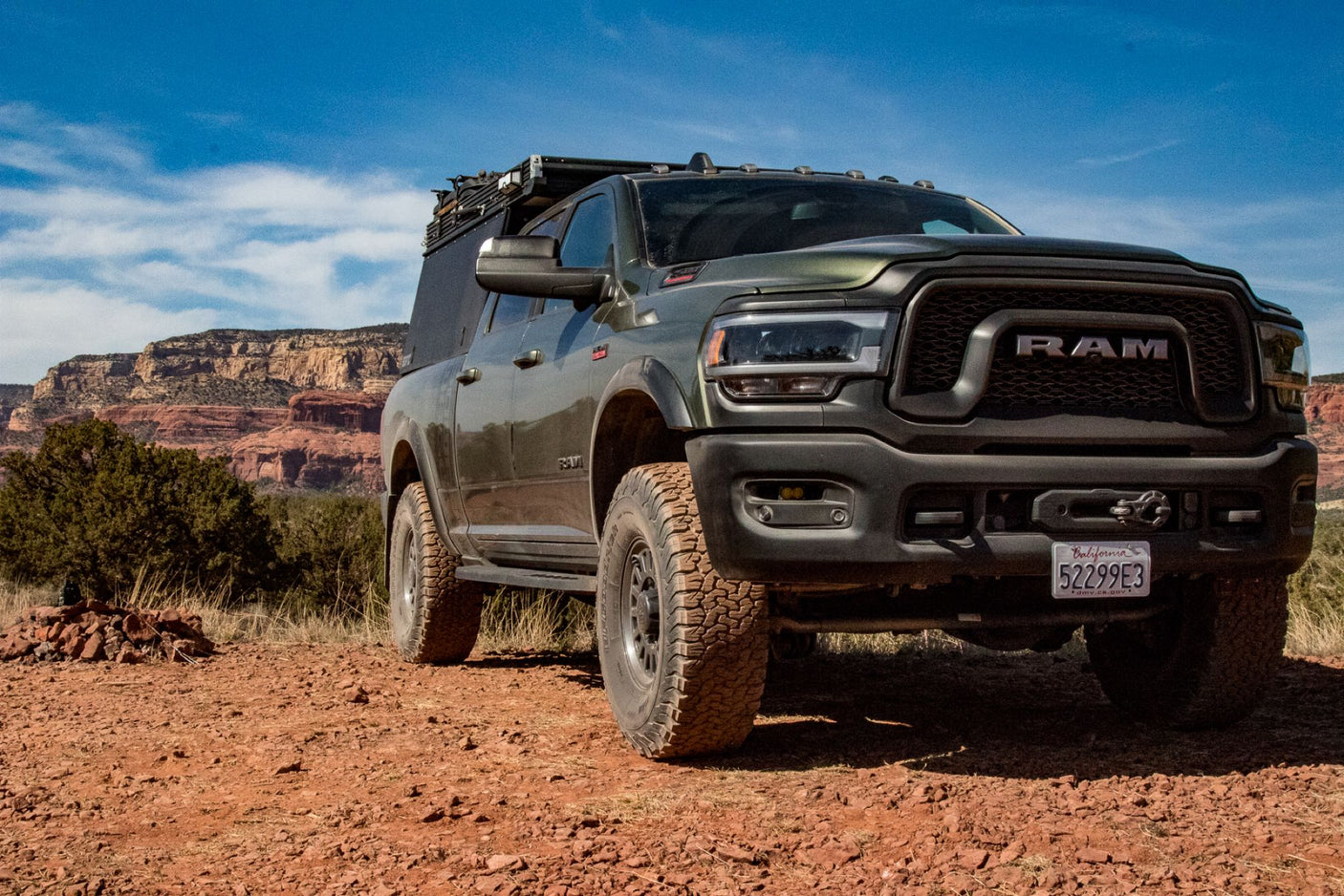 Rugged Ram truck with overland camper, ideal for an adventure rv rental. Parked on red dirt with striking red rock formations in the background.
