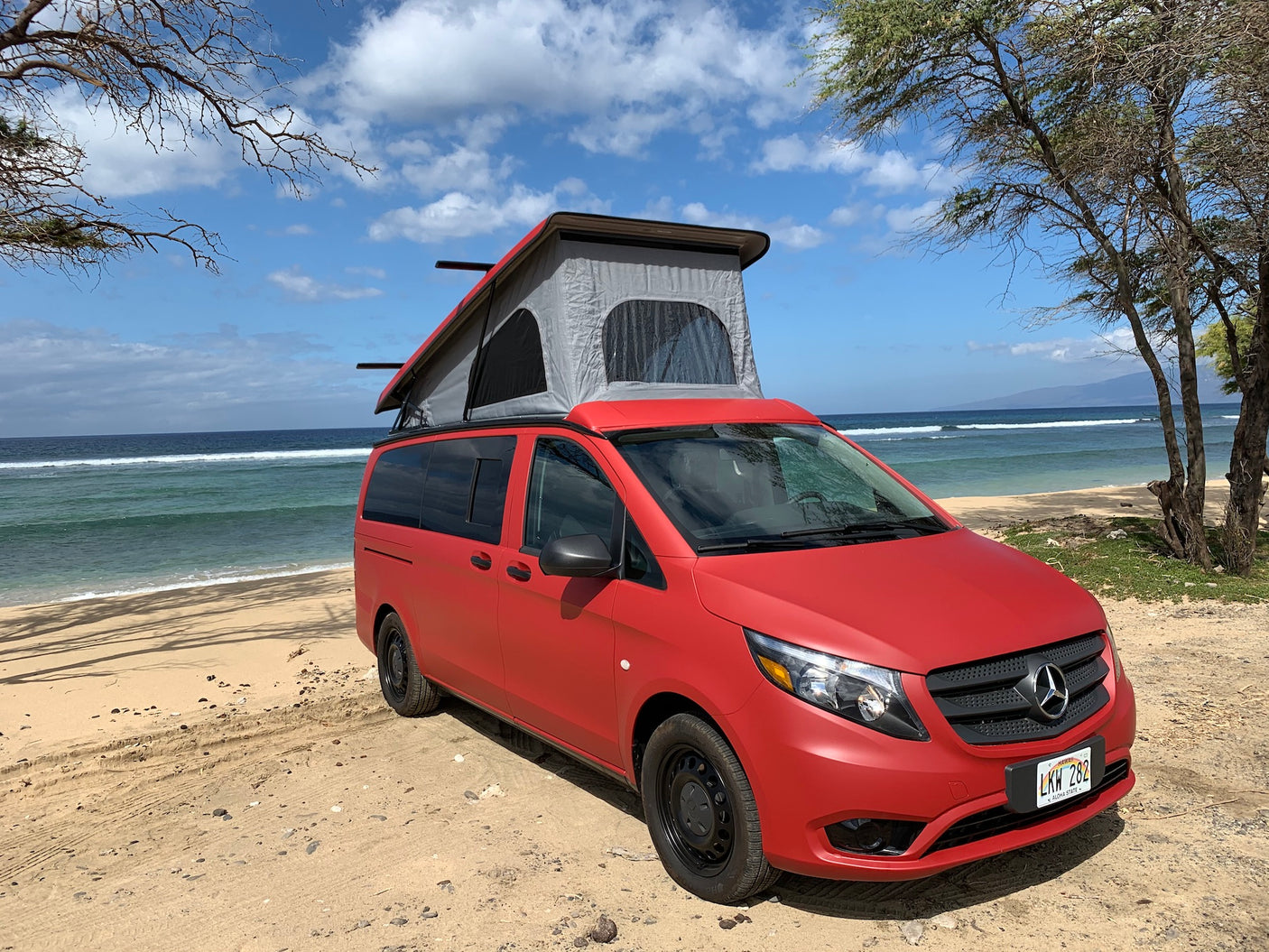 Red Mercedes pop-top camper van RV rental on a sandy Hawaiian beach. Perfect for ocean adventures.