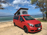 Red Mercedes pop-top camper van RV rental on a sandy Hawaiian beach. Perfect for ocean adventures.