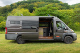 Gray Ram ProMaster camper van, ideal for RV rental adventures, parked on grass with its side door open showing the interior kitchen.