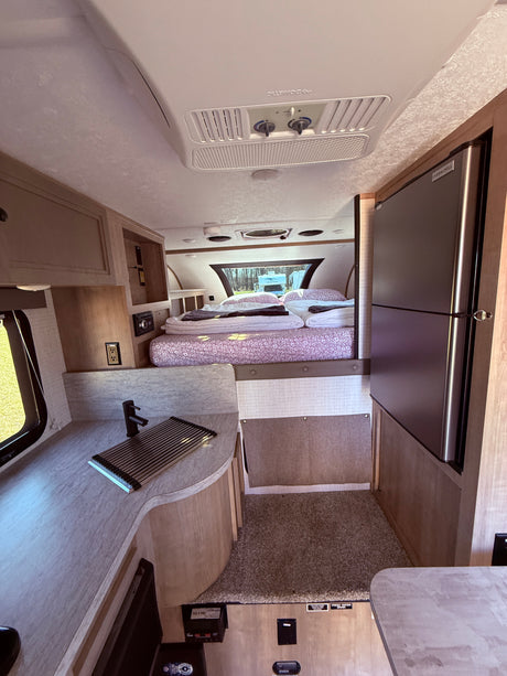 Spacious RV rental interior showcasing a modern kitchen with sink, large refrigerator, and a cozy bedroom with patterned bedding.