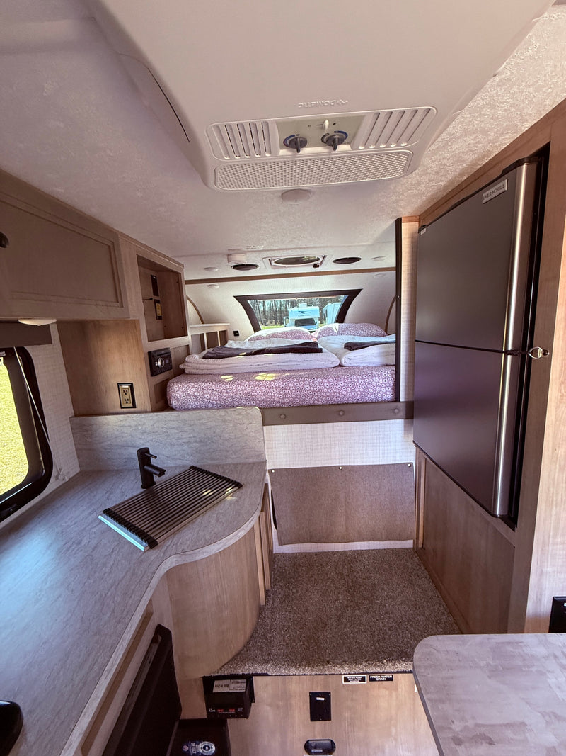 Spacious RV rental interior showcasing a modern kitchen with sink, large refrigerator, and a cozy bedroom with patterned bedding. — photo 16