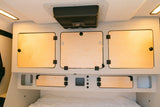 Modern Escapod rv rental interior with wooden cabinets, ceiling fan, and controls above a bed.