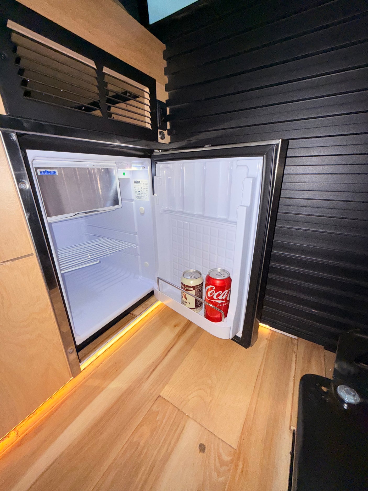 This RV rental shows an open Isotherm mini-fridge with drinks, built into a compact wooden interior. Perfect for road trip snacks.