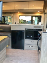 Modern RV rental interior: kitchen with sink, microwave, fridge, and cozy seating.