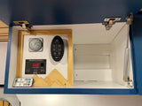 RV rental interior showing system controls: Victron energy monitor, tank levels, and fan remote in an open cabinet.