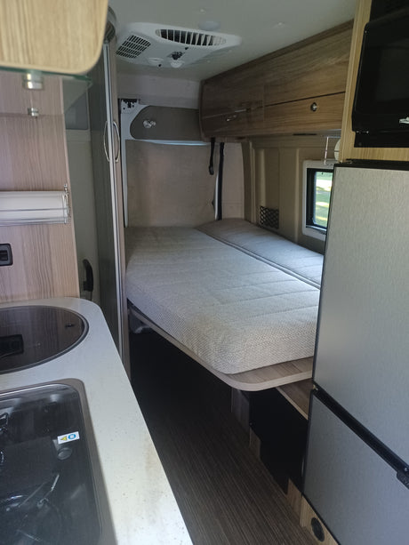 Inside an RV rental: a compact living space with a comfy bed, kitchen counter, sink, storage, and an AC unit.