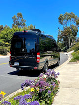 Black Mercedes-Benz Sprinter RV, an ideal rv rental for travel, parked on a scenic road with vibrant flowers.