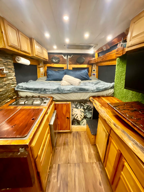Stylish RV rental camper van with a cozy bed, compact kitchen, rustic wood finishes, and unique wall textures.