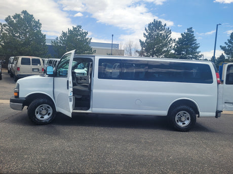 White extended passenger van with open door, parked on asphalt. Similar to vehicles in an rv rental fleet, ready for travel.