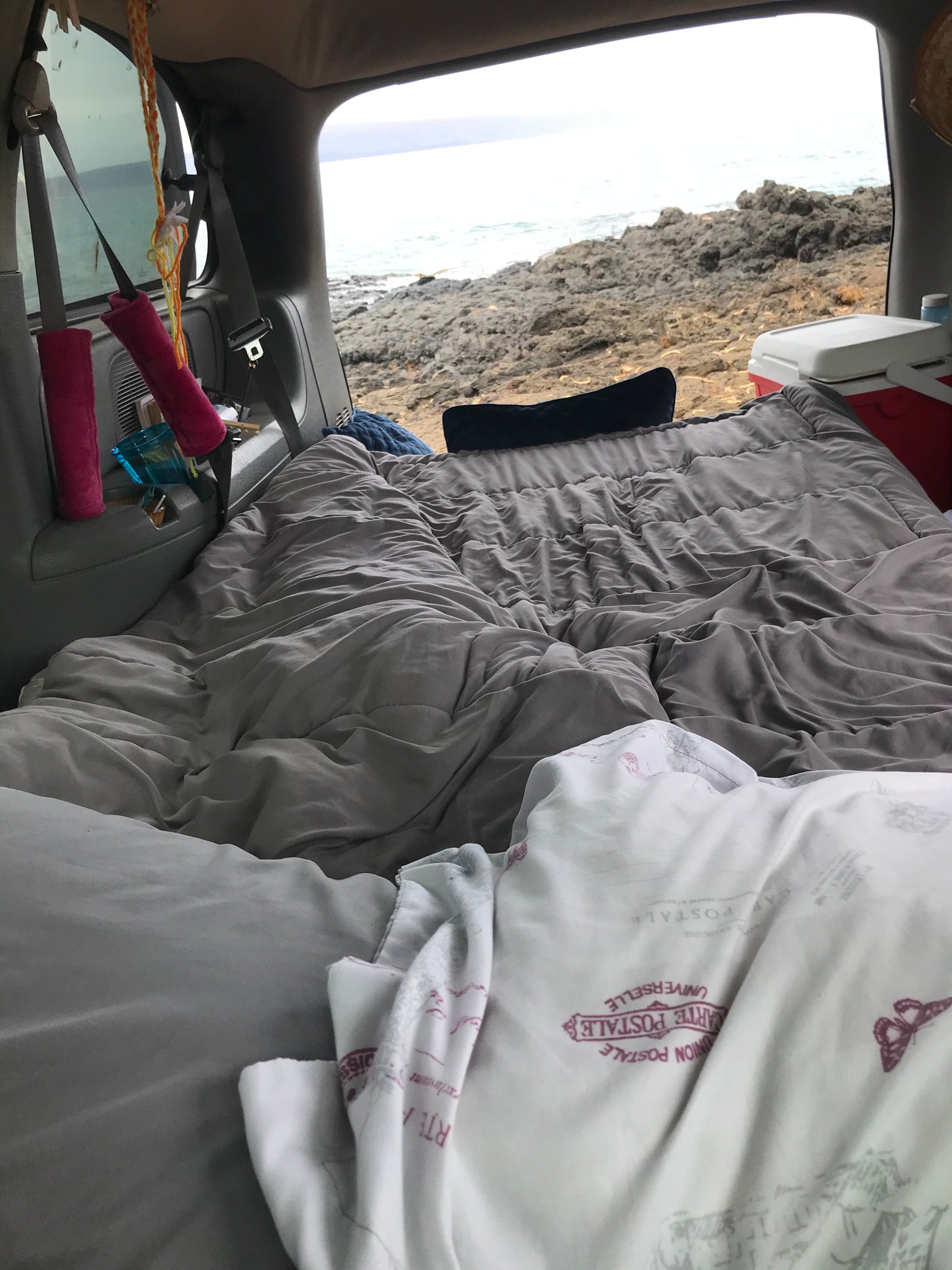 Inside a customized rv rental: a cozy bed with blankets and pillows, overlooking a rugged ocean coastline. Perfect for van life camping.