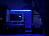 Bright blue LED lights illuminate this RV rental at night. The travel trailer's door is open, with steps leading inside for camping fun.