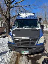 Blue Sprinter rv rental van, partially snow-covered, parked on a Minnesota street. Sunny winter day with bare trees.