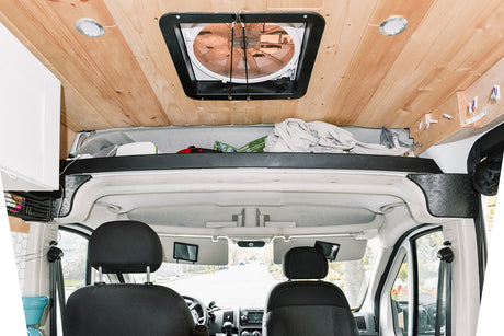 Interior view of an RV rental: wood ceiling with fan & lights, plus front cabin & clever overhead storage.