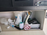 An RV rental's well-organized cabinet filled with a fan, cleaning supplies, and travel guides.