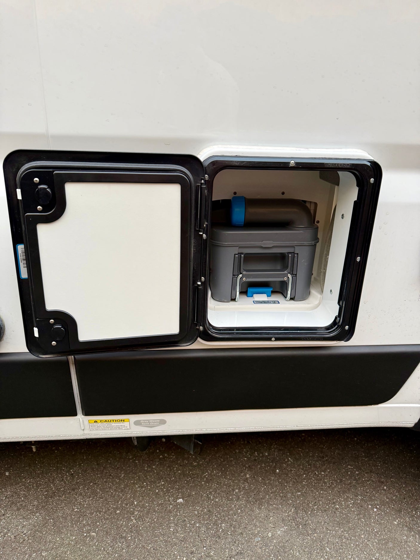RV rental: Exterior panel open on a white RV, showing a gray cassette toilet waste tank within the compartment.