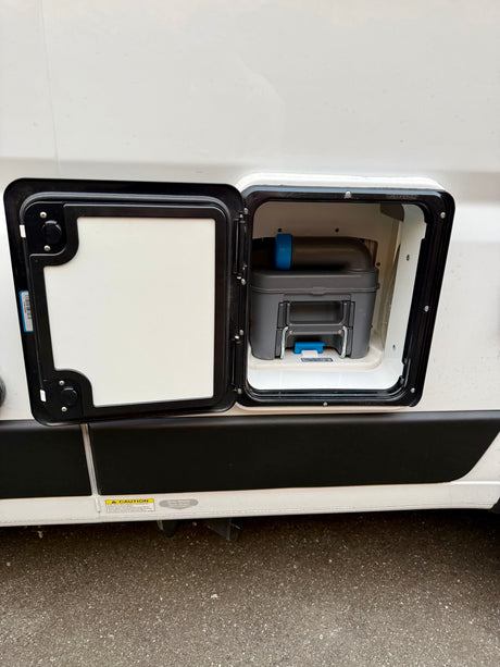 RV rental: Exterior panel open on a white RV, showing a gray cassette toilet waste tank within the compartment.
