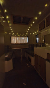 Cozy RV rental interior at night, illuminated by string lights, with kitchen cabinets and windows visible.