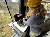 An RV rental kitchen with a person cooking eggs, an open screen door showing a natural outdoor scene with a turtle.