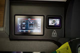 Inside an RV rental: a control panel with dual screens displaying fresh/gray tank levels, interior temp, and battery data.