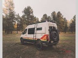 This white camper van, with colorful side stripes, is ideal for your next RV rental adventure in the serene forest.