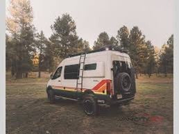 This white camper van, with colorful side stripes, is ideal for your next RV rental adventure in the serene forest.
