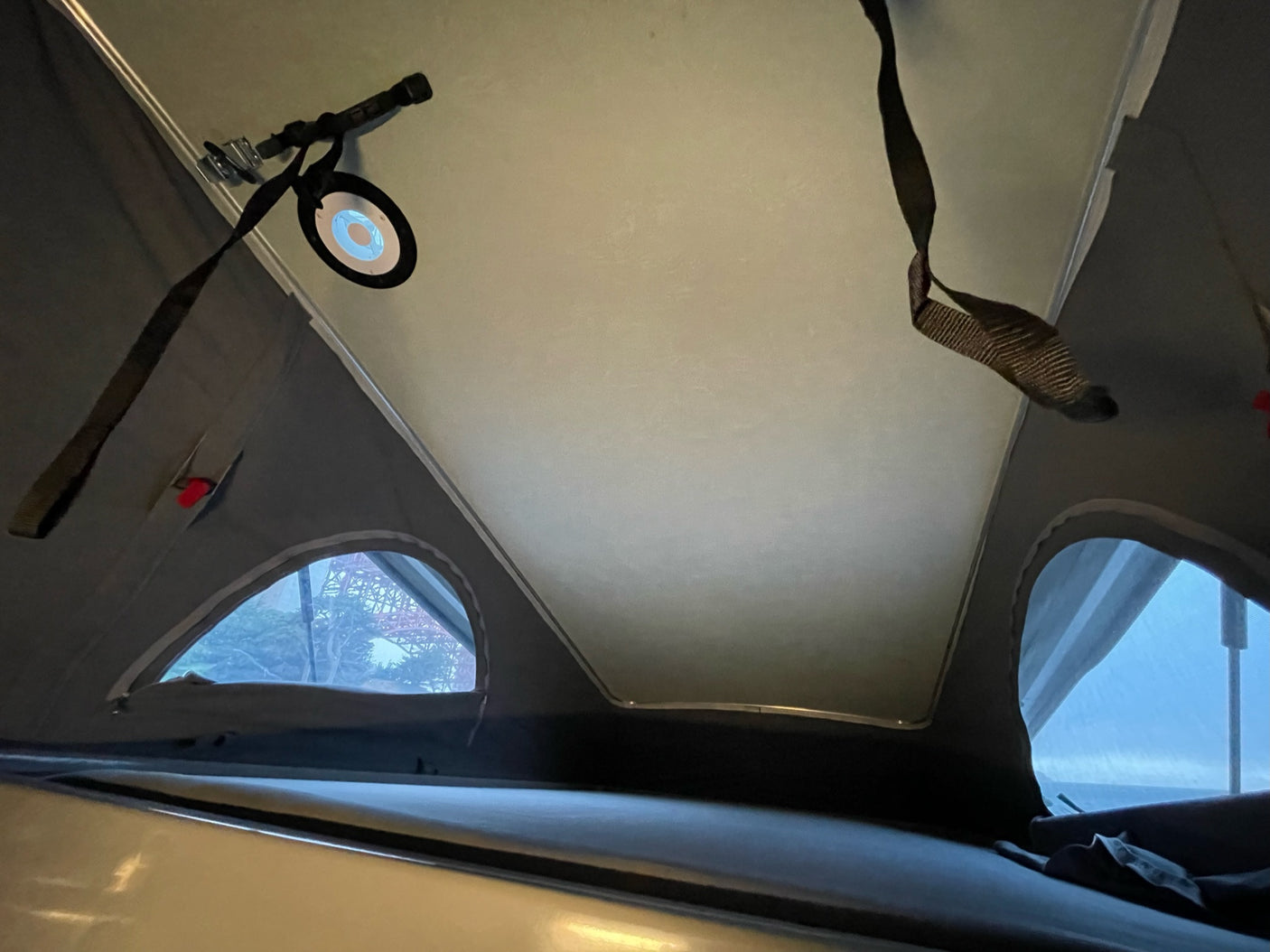Inside an RV rental pop-top: bright light, sleeping area, arched windows with bridge view. Perfect for adventures.