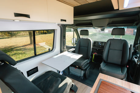 Modern RV rental van interior featuring a comfortable dining/workspace, swivel seats, and a large window.